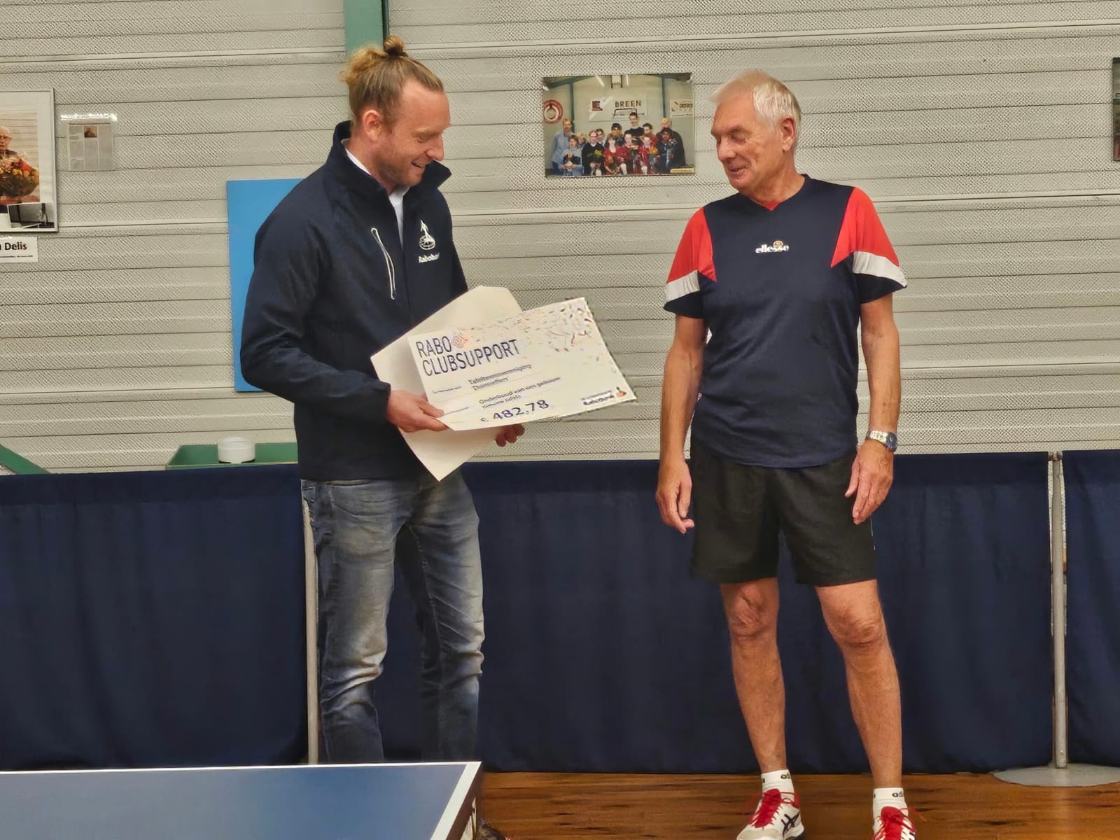 Een medewerker van de Rabobank bekijkt de cheque naast Ron Top